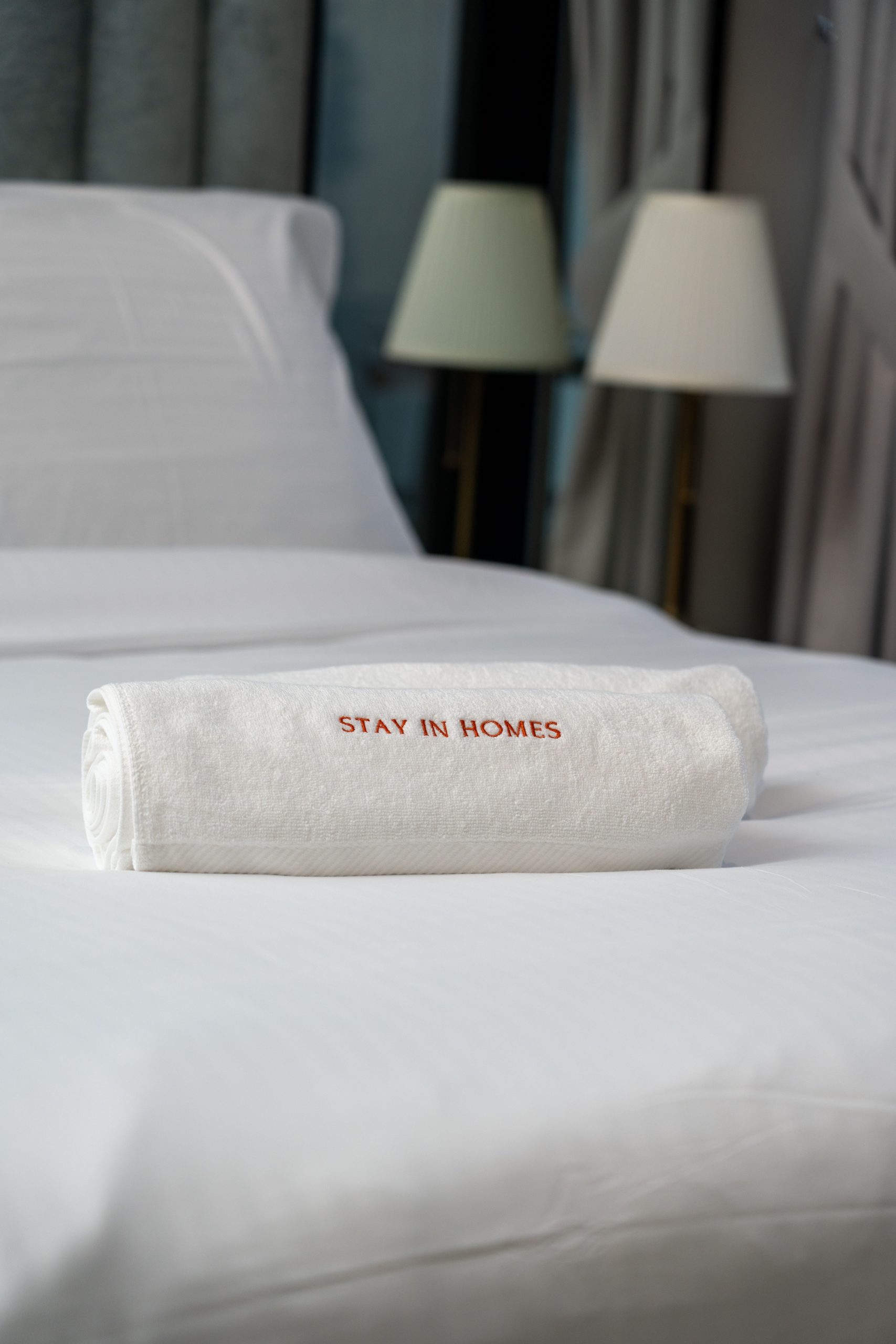 Elegant rolled towel with 'Stay in Homes' text on a pristine hotel bed indoors.