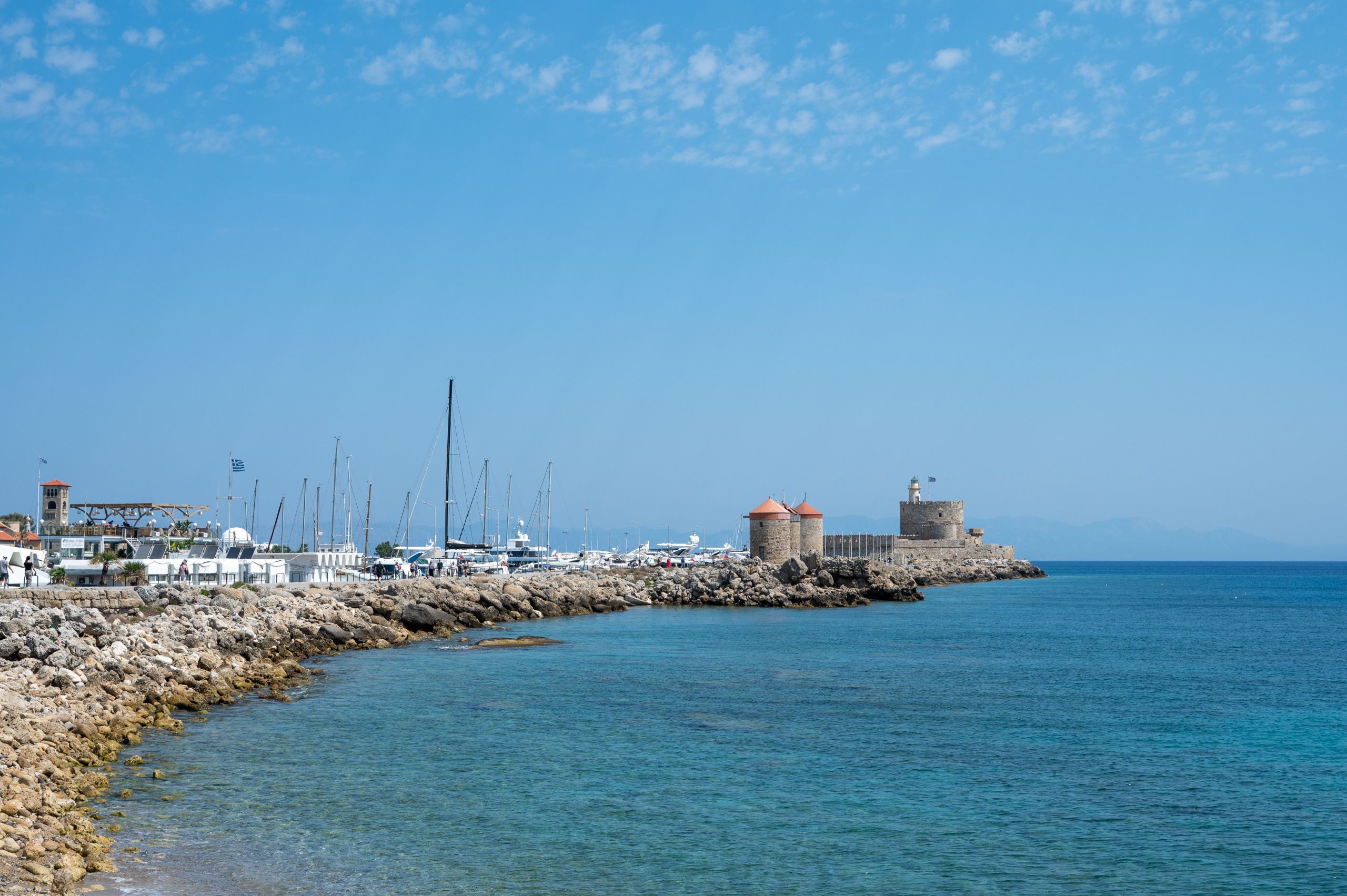 Crystal blue sea and Mandraki Harbor with Fort St. Nicholas in Rhodes, Greece.